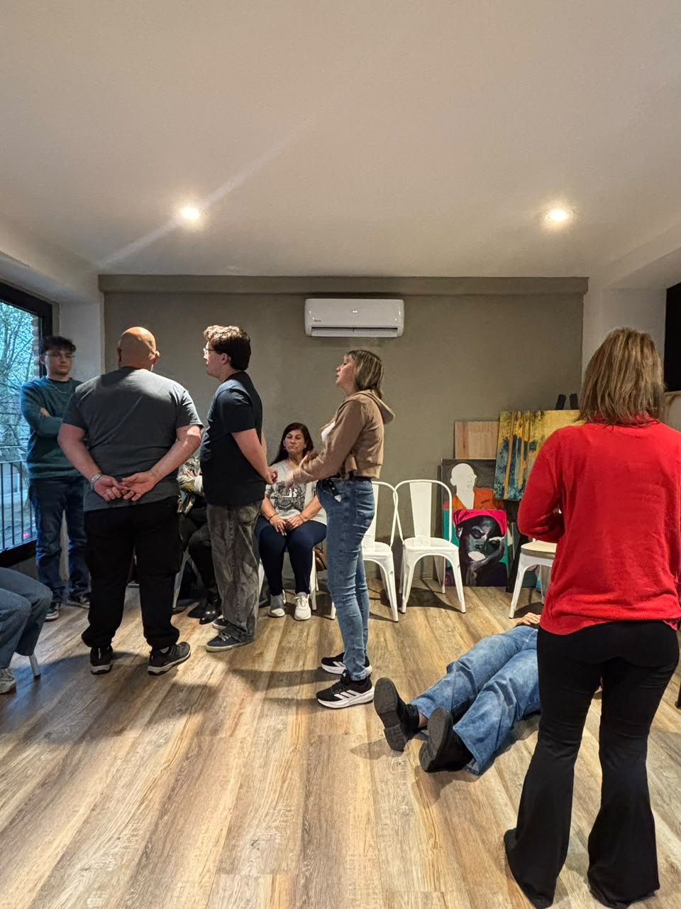 Representantes de pie en distintos lugares de la sala y una persona recostada en el piso, mientras el grupo observa sentado contra la pared.