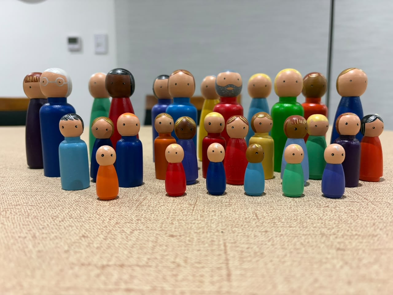 Muñecos de madera pintados a mano, de distintos tamaños y colores, agrupados sobre una mesa como una familia.